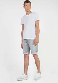 Witte t-shirt met korte mouwen gecombineerd met lichtgrijze opgerolde denimshorts en grijze sneakers. De outfit heeft een casual ontwerp.