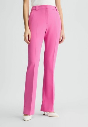 Pantaloni su misura rosa con una vestibilità slim e gambe dritte, caratterizzati da una texture liscia e tasche frontali; abbinati a tacchi bianchi a punta.