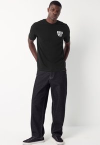 Black cotton T-shirt with "BEATLES" printed in white on the chest, paired with loose-fitting dark denim pants and black sneakers.