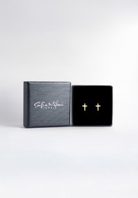 Boucles d'oreilles en or exposées dans une boîte à bijoux tapissée de velours noir avec un extérieur noir texturé et un logo en écriture blanche sur le couvercle.