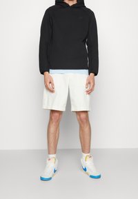 Svart huppetröja, ljusblå undertröja, vita shorts och vita sneakers med blå detaljer. Avslappnad atletisk outfit.