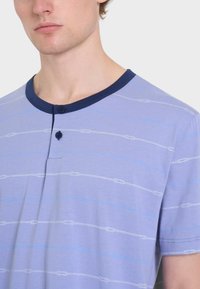 Maglietta corta viola chiaro con colletto blu navy. Presenta strisce orizzontali bianche e azzurre chiaro con motivi ad anello e due bottoni.