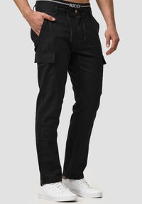 Black cargo pants with a drawstring waist, four pockets, and a sleek fit. Made from durable fabric, paired with white sneakers.