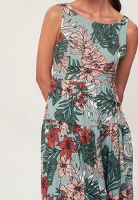 Floral Kleid mit einem blau-grünen Hintergrund und pinken sowie roten tropischen Mustern, einem enganliegenden Oberteil und einem ausgestellt ausgestellten Rock.