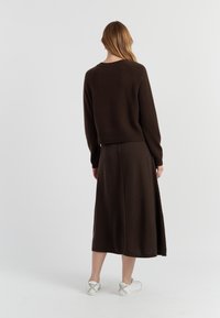 Donkerbruine gebreide trui met ribbels aan de onderkant en lange mouwen, gecombineerd met een bijpassende maxi-jurk, gedragen met witte sneakers.