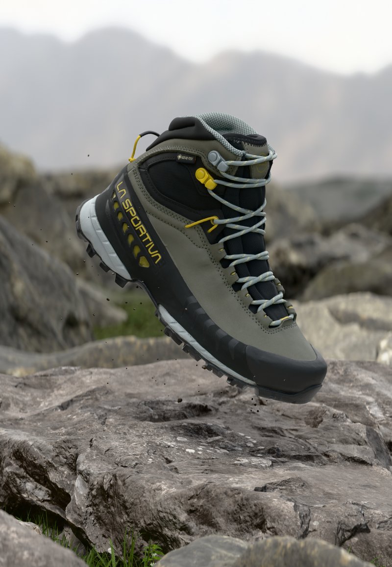 Stivale da hiking grigio e nero con tomaia impermeabile, suola in gomma, dettagli gialli e lacci grigi, posizionato sopra una superficie rocciosa.