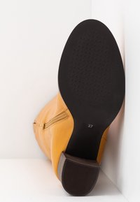 Botte cheville en cuir jaune avec une fermeture éclair latérale, semelle texturée et talon bloc marron. Taille 37 indiquée sur la semelle.