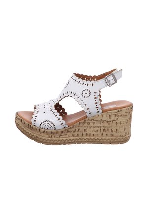 White espadrille wedge sandal featuring perforated floral design, brown leather insole, and a cork-textured sole. Adjustable ankle strap included.