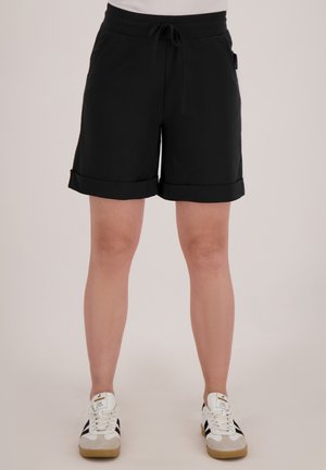 Zwarte shorts van een zacht materiaal, met een verstelbare tailleband en omslag aan de onderkant. Gecombineerd met witte sneakers met zwarte accenten.