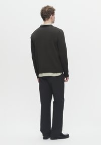Dark green knit sweater with a ribbed hem and cuffs, layered over a light green and white striped shirt, paired with black trousers.