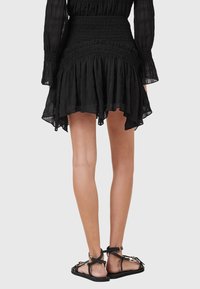 Abito midi nero, texturizzato, con vita arricciata e orlo a balze. Abbinato a sandali neri flat con dettagli a strisce.
