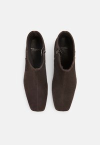 Brūni zamšādas potītes zābaki ar elegantu dizainu, plūstošu tekstūru, smailu purngalu un sānu rāvējslēdzēju aizdarei.