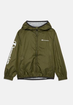 Veste légère vert olive avec capuche, poignets élastiques et fermeture éclair. Présente un logo blanc "Champion" sur la poitrine gauche et la manche.