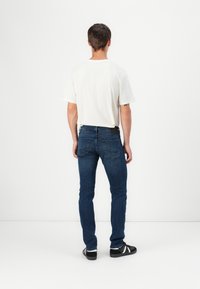 Bílý tričko s krátkým rukávem spárované s tmavě modrými slim-fit džíny. Černé boty s bílými pruhy. Viditelné detaily zadní kapsy.