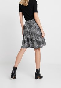 Svart figurnära topp med korta ärmar, kombinerad med en knälång kjol i svart och vitt mönster. Bärs med svarta ankelskor med en kraftig klack.