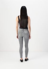 Jeans ajustados grises de cintura alta, con dos bolsillos traseros y dobladillos deshilachados. Combinados con una blusa sin mangas negra y zapatos oscuros.