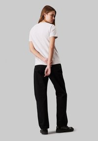 Camiseta de algodón gris claro, de mangas cortas, con escote redondo, combinada con pantalones negros de talle alto. Modelo de espaldas, fondo oscuro.