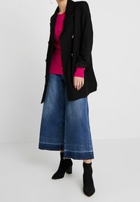 Musta kaksirivinen bleiseri, vaaleanpunainen neuletoppi, leveälahkeiset siniset farkkukulotit ja mustat nilkkurit. Sileät tekstuurit ja kontrastoivat värit.