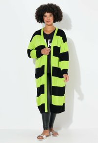 Cardigan lungo con ampie righe nere e verdi fluorescenti, caratterizzato da un'apertura frontale, due tasche e polsini a costine. Tessuto in maglia leggero.