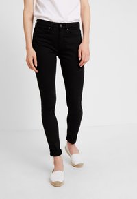 Svarta slim fit-jeans med midjehöjd, fem fickor och knappstängning. Matchade med vita espadrillos, med uppvikta fållar synliga.