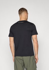 Sort kortærmet t-shirt med rund halsudskæring og trykt tekstdetalje på den øverste ryg. Fremstillet af et blødt, åndbart materiale.