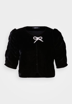 Casaco cropped de veludo preto com mangas curtas em puff, apresentando um detalhe de laço metálico na frente e um decote redondo.