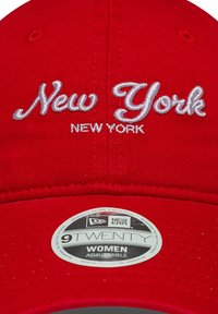 Căciulă de baseball roșie cu broderie "New York" în alb, având o coroană structurată și mărime ajustabilă. Include o etichetă cu logo-ul "New Era".