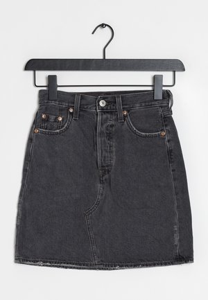 Jupe en denim noir avec poches avant et fermeture par boutons, suspendue sur un cintre noir sur fond blanc.