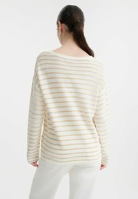 Maglione crema con sottili righe beige, maglia leggera, scollatura ampia, vestibilità morbida, maniche lunghe. Indossato con pantaloni chiari.
