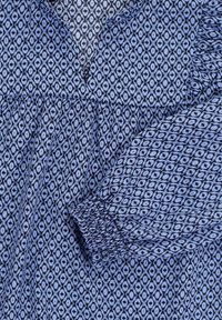 Blauwe blouse met een patroon met diamanten, met een geplooide halslijn en elastische mouw cuffs. De stof heeft een zachte textuur en een subtiele glans.