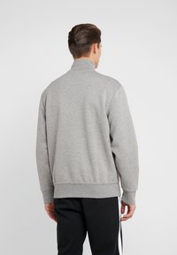 Šedá mikina s vysokým límcem a žebrovanými manžetami, vyrobená z jemného materiálu, má jednoduchý design, detailní švy a volný střih.