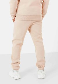 Lichtroze joggings met elastische boorden en een comfortabele pasvorm, gecombineerd met witte sneakers met geperforeerde details. Glad en fijn textiel.