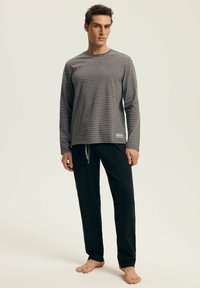 Graues gestreiftes Langarmoberteil mit Rundhalsausschnitt, kombiniert mit schwarzen Jogginghosen mit Kordelzug in lockerer Passform. Weicher Stoff, minimalistische Details.