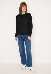 Maglione nero testurizzato con maniche lunghe abbinato a jeans a gamba larga blu e sneakers bianche con accenti neri. Design semplice e moderno.