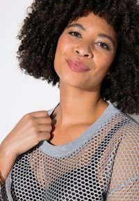 Maglione grigio in rete con un ampio scollo e maniche corte. Il tessuto presenta un motivo a nido d'ape, rivelando la pelle sottostante.