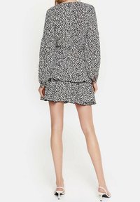 Svartvit blommig klänning med lång ärm, volangkant och figursydd överdel. Tyget har ett litet blommönster och en mjuk textur.