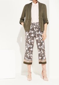 Blazer vert olive au design simple, chemise rose à col, et pantalon cropped à motifs avec des paisleys dans des tons beige et marron. Talons d'un rose pâle.