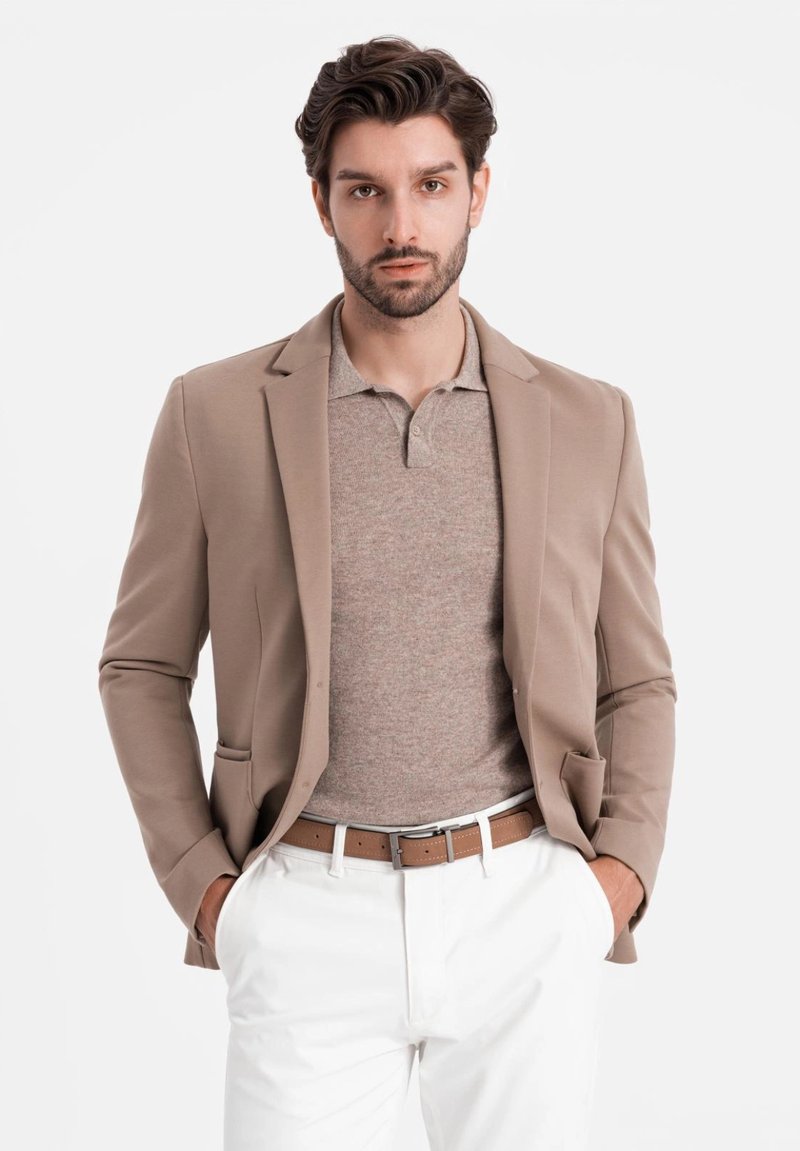 Beiger Blazer über einem hellbraunen Polohemd, weißen Hosen und einem braunen Gürtel. Glatte Stoffqualität mit taillierter Passform und subtilen Details.