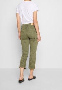 Olive green cropped trousers with embroidered scalloped hem. Made of a soft, stretch fabric; features a standard back pocket and belt loops.