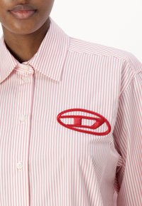 Striped shirt in pink and white, featuring a red embroidered logo on the left chest, with a collar and button closure.