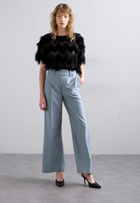 Czarny, futrzasty crop top w zygzakowaty wzór; jasnoniebieskie szerokie spodnie; czarne spiczaste szpilki. Gładkie tekstury z kontrastującymi materiałami.