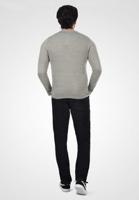 Camisa gris de manga larga combinada con pantalones vaqueros negros. La camisa tiene un estilo ajustado, y los pantalones son de corte slim con un diseño clásico. Zapatillas negras visibles.