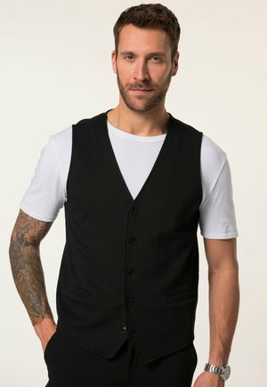 Schwarze Weste mit einem V-Ausschnitt-Design, fünf Knöpfen und zwei seitlichen Taschen. Über einem weißen T-Shirt getragen. Hat eine glatte Stoffoberfläche.