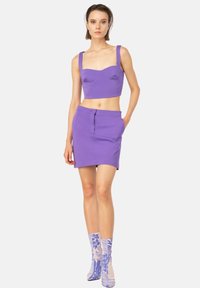 Top corto viola con spalline larghe, coppe imbottite e una mini gonna alta coordinata. Il modello indossa calzini blu a fantasia con un design floreale.