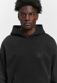 Black hooded sweatshirt made of soft fabric, featuring a front pocket and a subtle graphic on the chest with the text "RETERNITY."