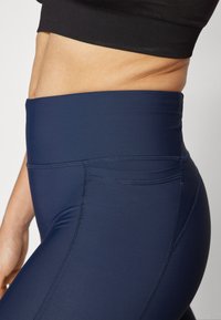 Høyt livet marineblå leggings laget av glatt, elastisk stoff med flatlock-sømmer og en subtil, matt finish. Har en bred midje.