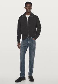 Gray zip-up sweater with a high collar, worn over a white t-shirt, paired with faded blue jeans and black ankle boots.