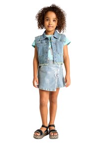 Gilet in denim con orlo sfrangiato, T-shirt azzurra con stampa, gonna in denim azzurra con dettagli a bottone e sandali neri con accenti intrecciati.