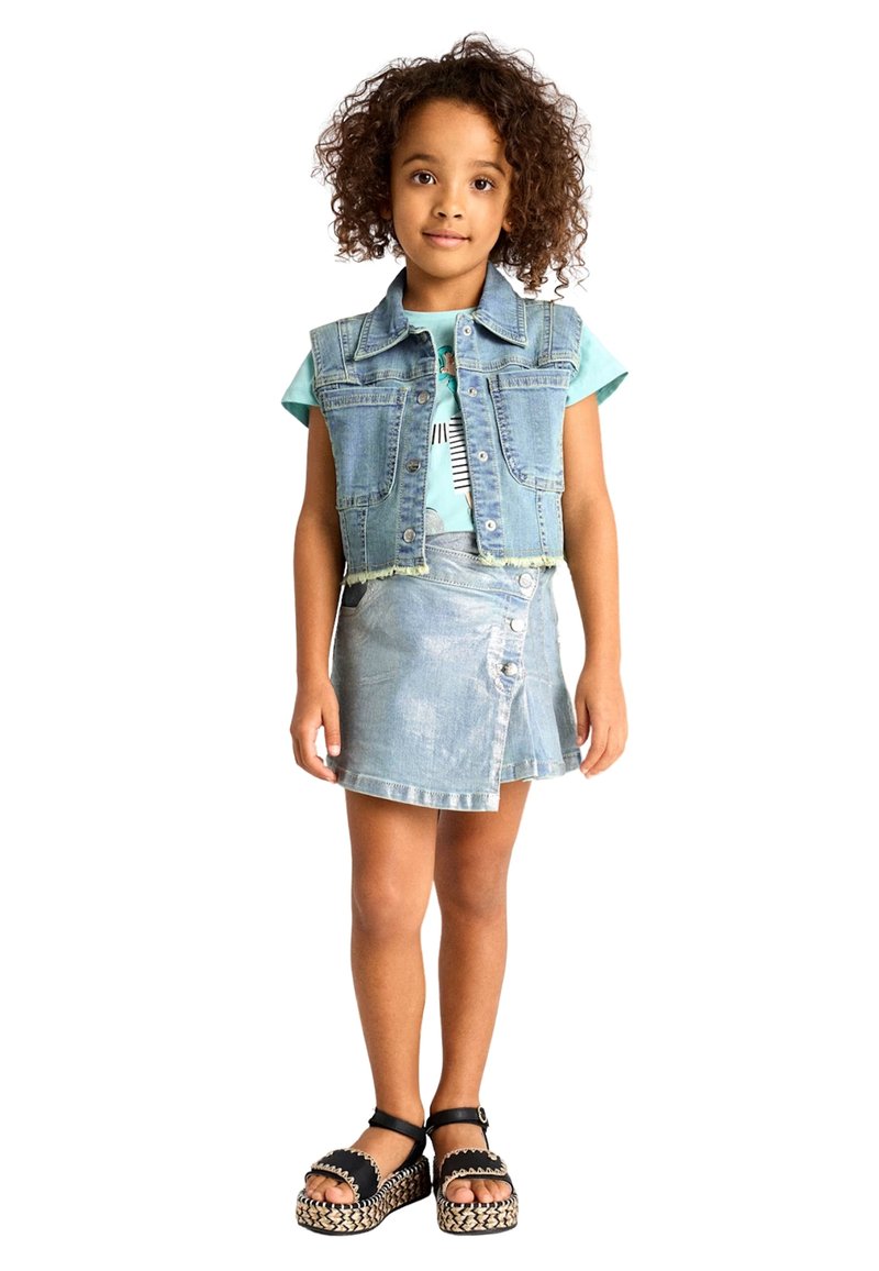 Gilet in denim con orlo sfrangiato, T-shirt azzurra con stampa, gonna in denim azzurra con dettagli a bottone e sandali neri con accenti intrecciati.