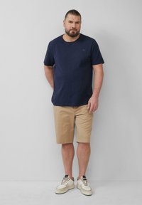 Navyblauwe T-shirt met korte mouwen, gecombineerd met beige shorts. Casual witte sneakers met beige accenten. Eenvoudig, relaxed fit ontwerp.